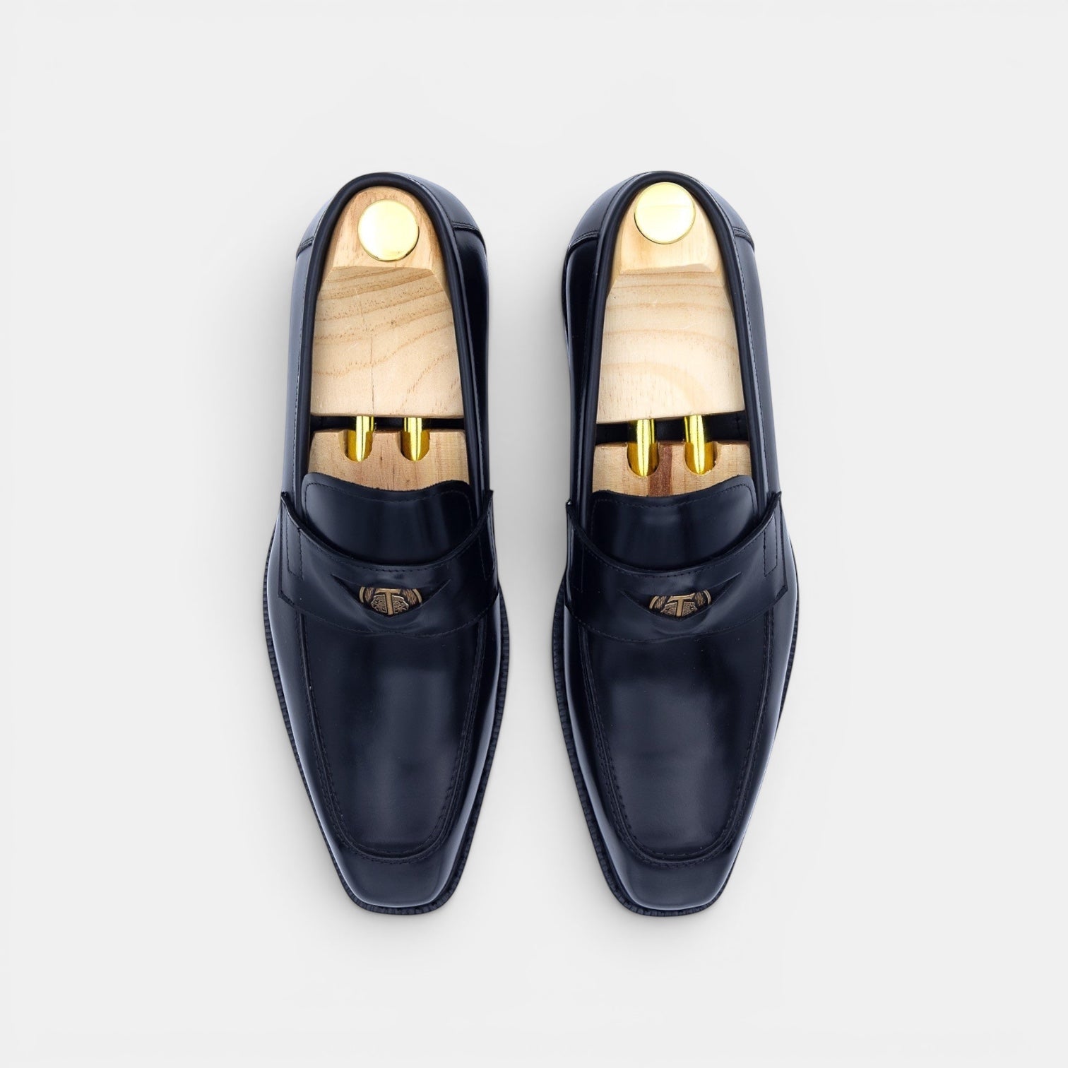 Barcon Getta Inc black leather penny loafers with metal accent and square toe, displayed on shoe trees.