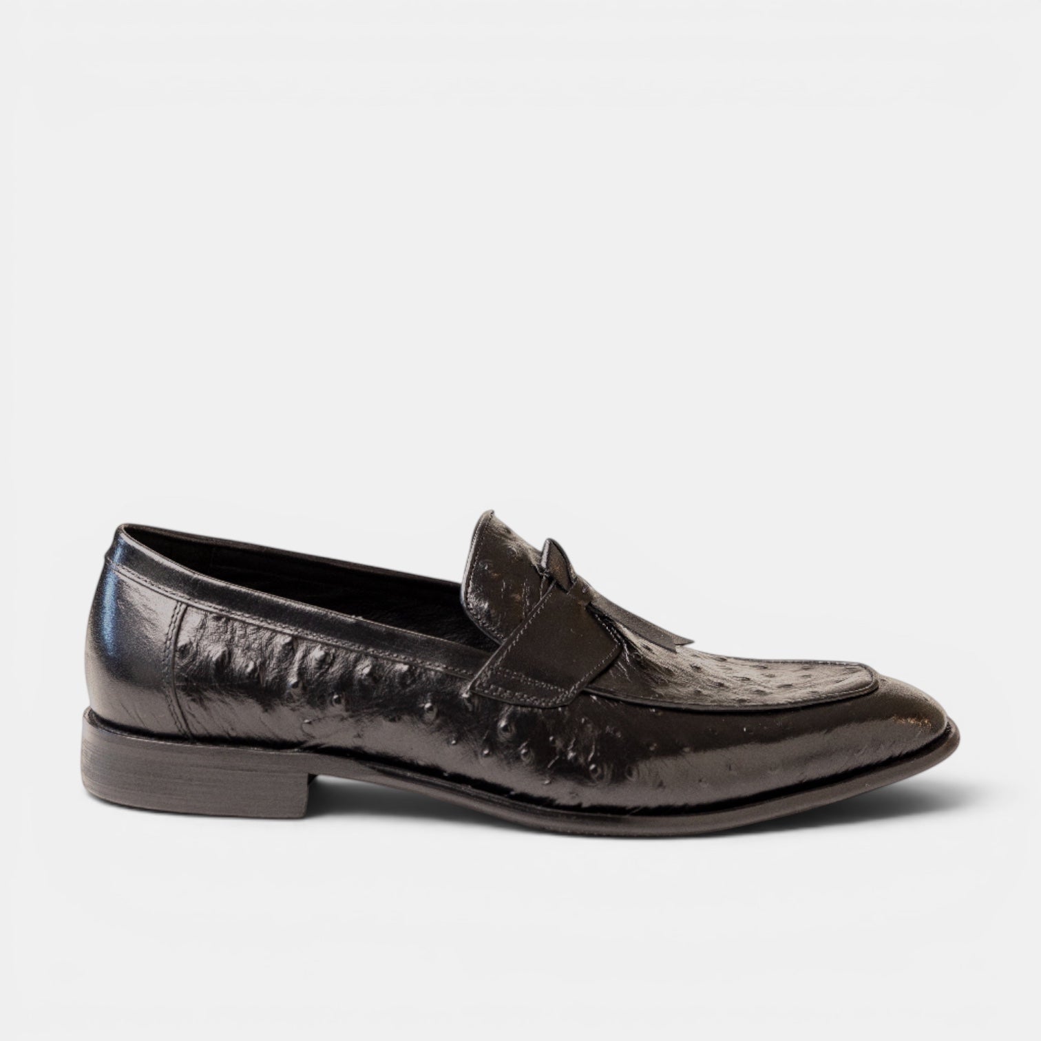 Barcon Getta Inc black ostrich-embossed leather kiltie tassel loafer with a pointed toe and stacked heel.