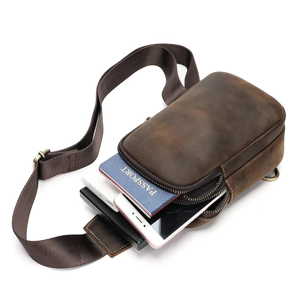 Barcon Getta Inc TRAVERSE cross-body bag in distressed brown leather with adjustable strap and multiple pockets, holding a passport, phone, and power bank.
