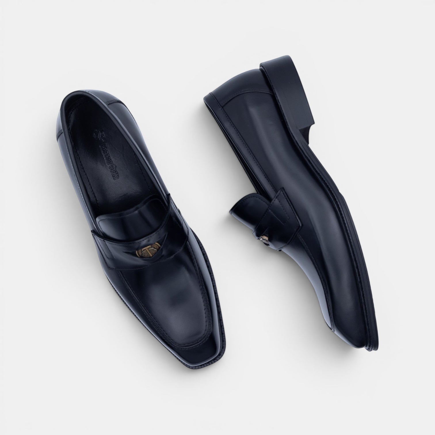 Barcon Getta Inc black leather penny loafers with metal accent detail and square toe.